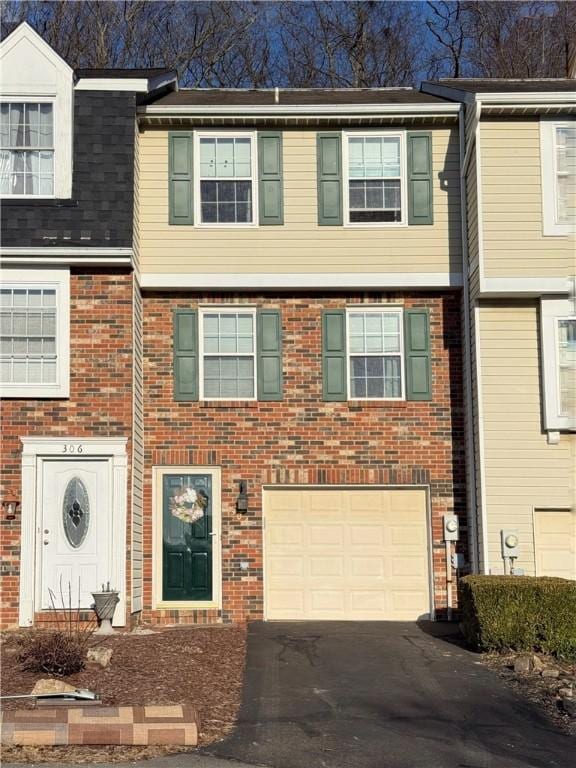 townhome / multi-family property with a garage, aphalt driveway, and brick siding