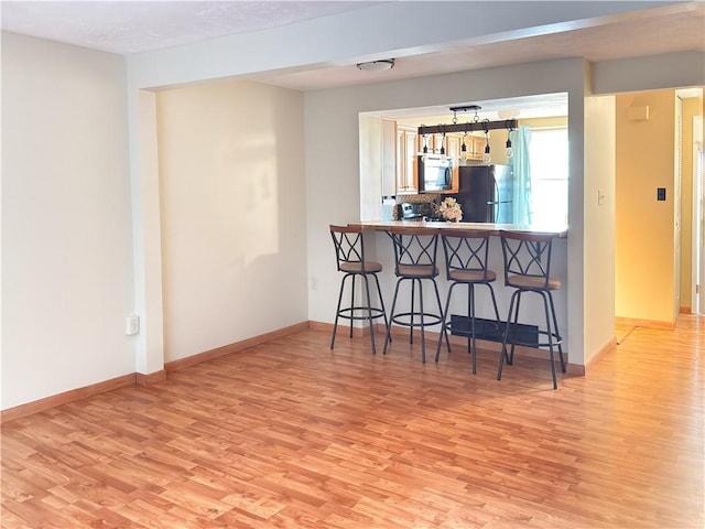 kitchen with light wood-type flooring, a kitchen breakfast bar, and freestanding refrigerator