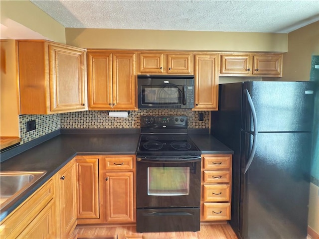 kitchen featuring a sink, backsplash, black appliances, light wood finished floors, and dark countertops