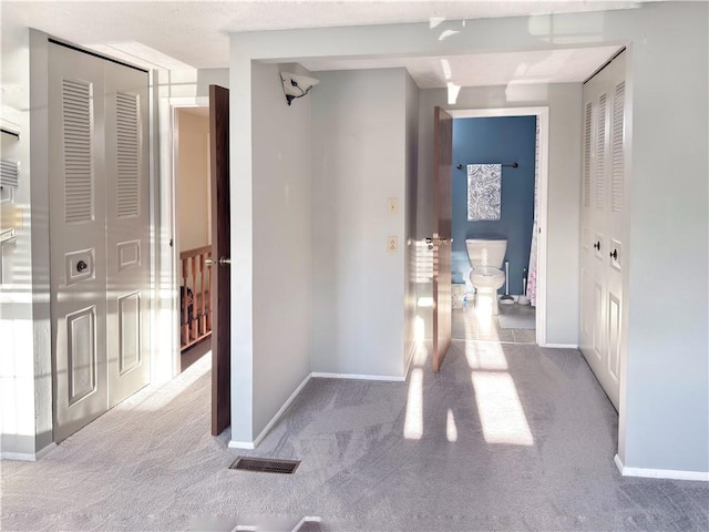 corridor featuring carpet floors, visible vents, and baseboards