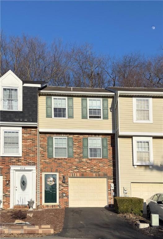 townhome / multi-family property featuring a garage, driveway, and brick siding