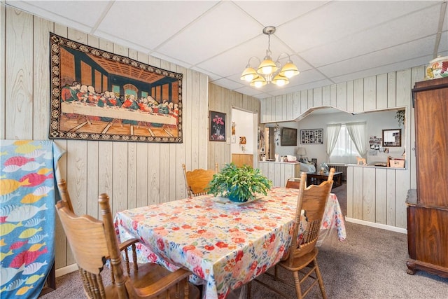 dining space with a paneled ceiling, carpet floors, wooden walls, and a chandelier