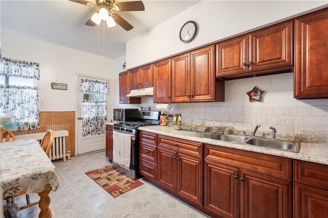 kitchen featuring a wainscoted wall, light countertops, stainless steel gas stove, a sink, and under cabinet range hood