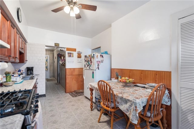 kitchen featuring stainless steel gas stove, brown cabinetry, ceiling fan, freestanding refrigerator, and light countertops