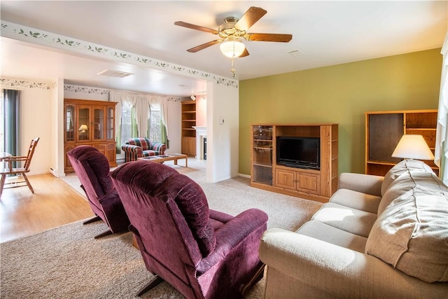 living area featuring a fireplace, visible vents, light carpet, ceiling fan, and baseboards