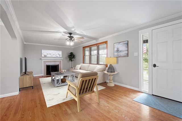 living area with light wood-style floors, a tiled fireplace, baseboards, and crown molding