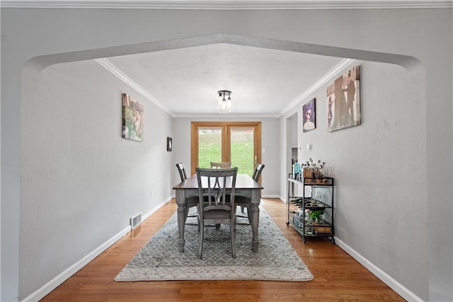 dining area with light wood-type flooring, baseboards, visible vents, and ornamental molding