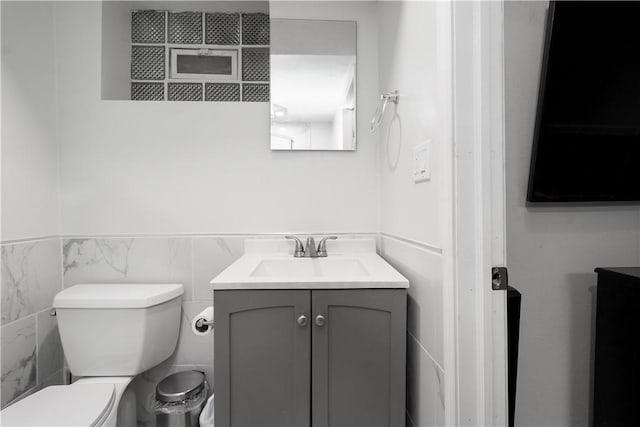 half bath featuring toilet, wainscoting, tile walls, and vanity