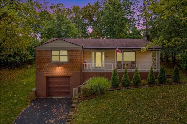 view of front of home featuring aphalt driveway, covered porch, a garage, brick siding, and a lawn