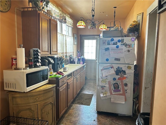 kitchen with white appliances, a sink, light countertops, brown cabinets, and decorative light fixtures