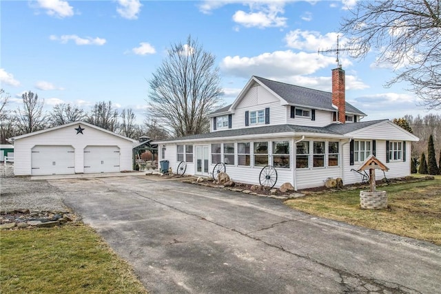 view of front facade featuring a garage, a sunroom, a chimney, and an outbuilding