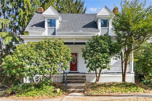 view of front of house with a shingled roof, a chimney, and a porch