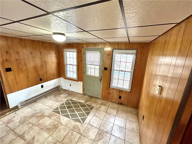 doorway with a baseboard radiator, a drop ceiling, and wooden walls