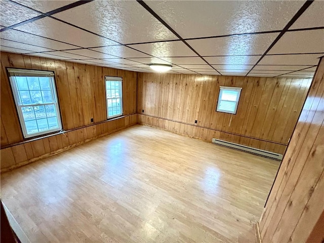 spare room featuring a paneled ceiling, baseboard heating, wood finished floors, and a wealth of natural light