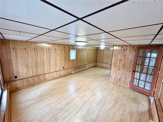 below grade area with a paneled ceiling, light wood finished floors, a baseboard radiator, and wooden walls