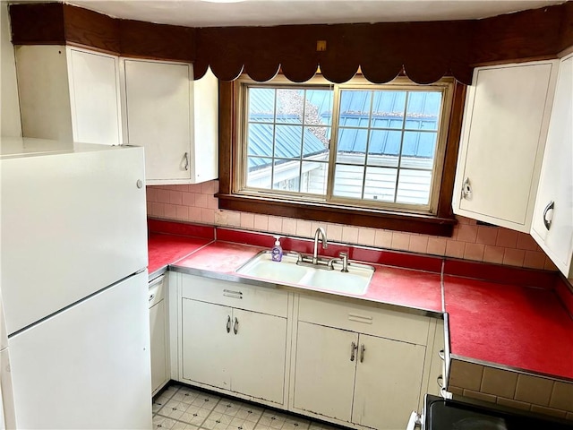 kitchen featuring tasteful backsplash, freestanding refrigerator, light floors, white cabinetry, and a sink