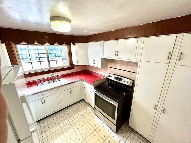 kitchen featuring decorative backsplash, white cabinets, electric stove, light floors, and a sink