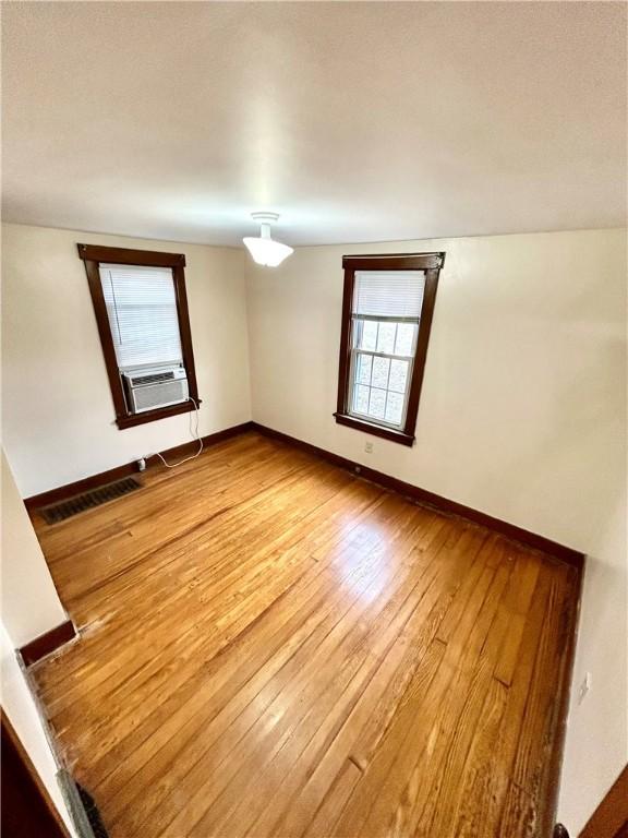 unfurnished room with hardwood / wood-style floors, baseboards, visible vents, and cooling unit