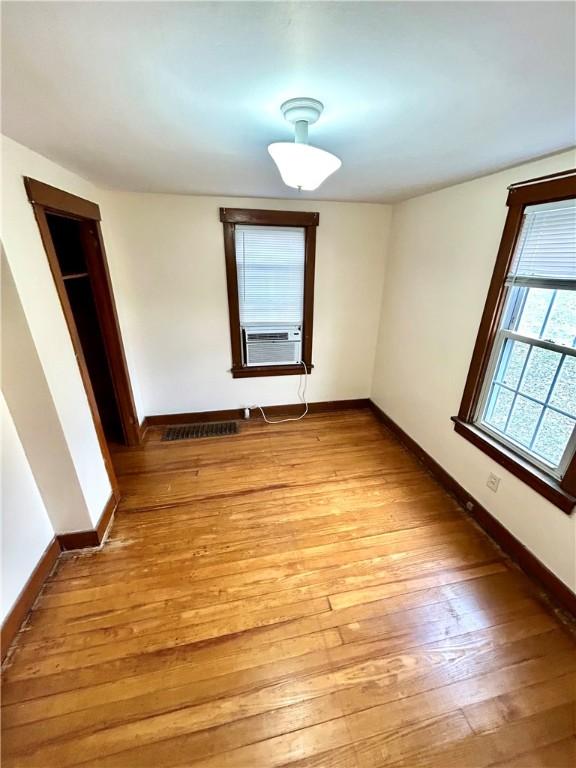 unfurnished room with cooling unit, light wood-style flooring, and baseboards