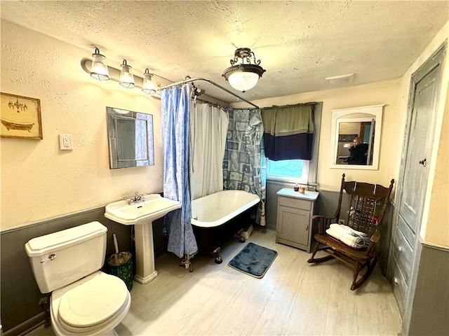 bathroom with a soaking tub, a textured ceiling, toilet, and wood finished floors