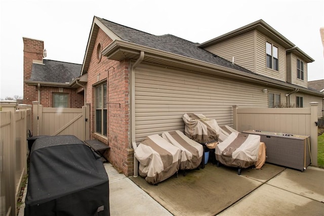 rear view of property featuring brick siding, fence, roof with shingles, a gate, and a patio area