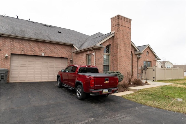 view of side of home featuring driveway, a shingled roof, a chimney, a gate, and brick siding