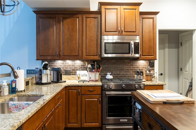 kitchen with stainless steel appliances, a sink, backsplash, and light stone countertops