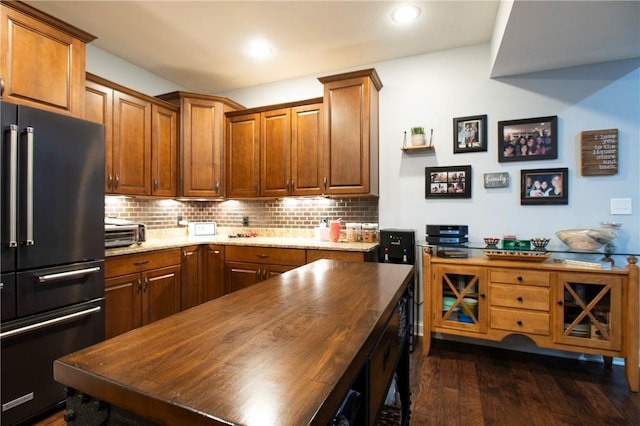 kitchen with dark wood-style floors, high end fridge, brown cabinetry, and backsplash