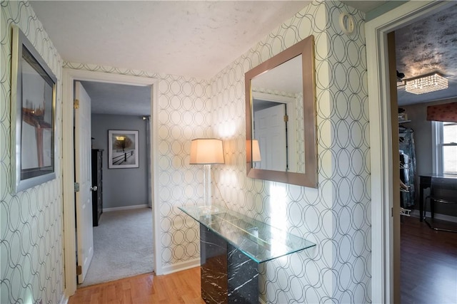 hallway featuring light wood-type flooring, wallpapered walls, and baseboards