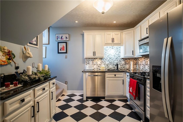 kitchen with a sink, white cabinets, appliances with stainless steel finishes, light floors, and dark countertops