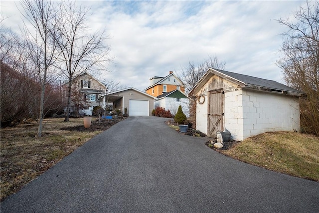 view of front facade with aphalt driveway, a detached garage, concrete block siding, and an outdoor structure