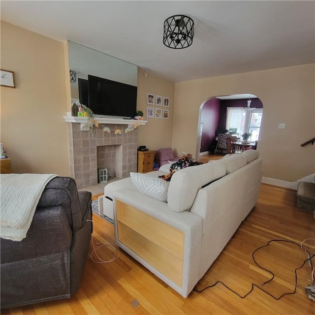 living room featuring baseboards, a tiled fireplace, arched walkways, and wood finished floors