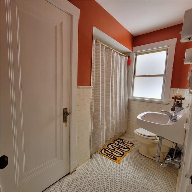 bathroom with a shower with shower curtain, a wainscoted wall, tile walls, and toilet