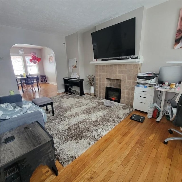 living room featuring arched walkways, a textured ceiling, a tile fireplace, baseboards, and hardwood / wood-style floors