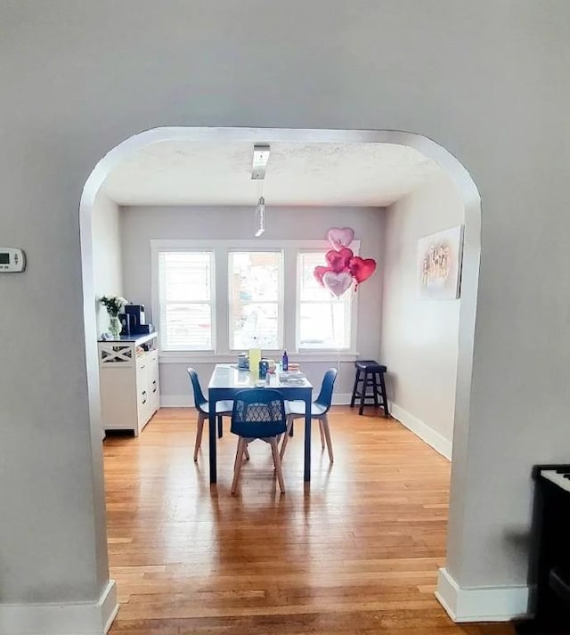 dining area with light wood finished floors, baseboards, and arched walkways