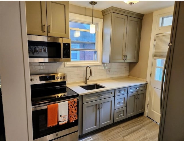 kitchen featuring gray cabinets, light countertops, decorative backsplash, appliances with stainless steel finishes, and a sink