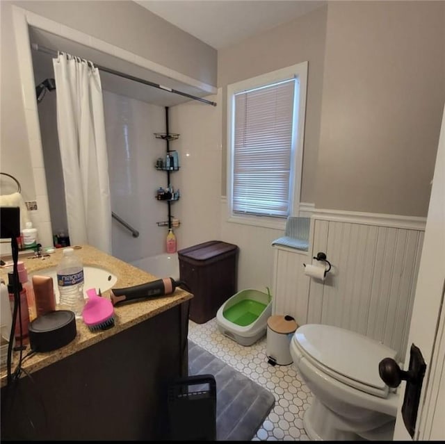 bathroom with a shower with shower curtain, wainscoting, vanity, and toilet