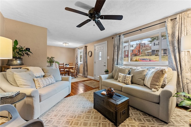 living room with ceiling fan, baseboards, a textured ceiling, and wood finished floors