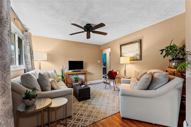 living area featuring a ceiling fan, a textured ceiling, baseboards, and wood finished floors