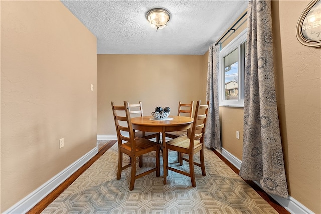 dining area with a textured ceiling, baseboards, and wood finished floors