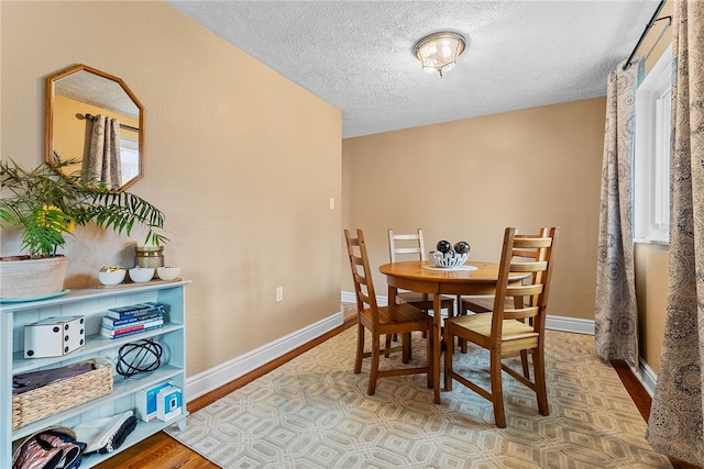 dining space featuring a textured ceiling, baseboards, and wood finished floors