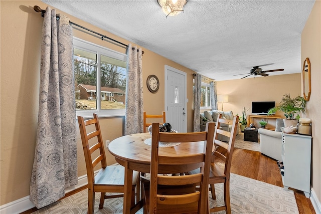 dining area with a textured ceiling, baseboards, a ceiling fan, and light wood-style floors