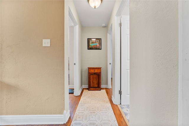 corridor featuring light wood finished floors, baseboards, and a textured wall