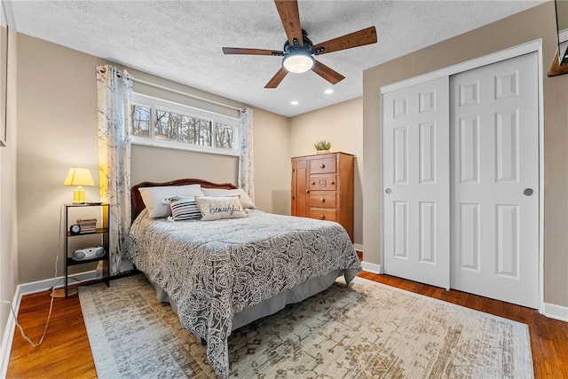 bedroom with a closet, a ceiling fan, a textured ceiling, wood finished floors, and baseboards