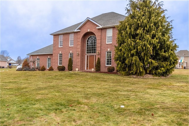 colonial home featuring a front yard, a shingled roof, and brick siding