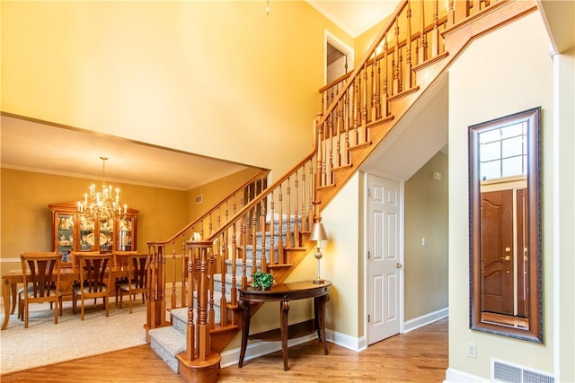 stairs with a notable chandelier, a high ceiling, wood finished floors, visible vents, and crown molding