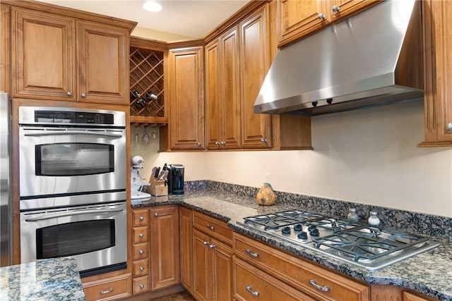 kitchen with dark stone counters, stainless steel appliances, brown cabinetry, and under cabinet range hood