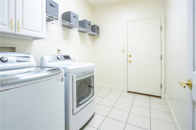 clothes washing area featuring light tile patterned flooring, washing machine and clothes dryer, cabinet space, and baseboards