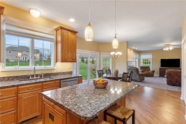kitchen with stainless steel dishwasher, brown cabinetry, a kitchen bar, a sink, and a center island