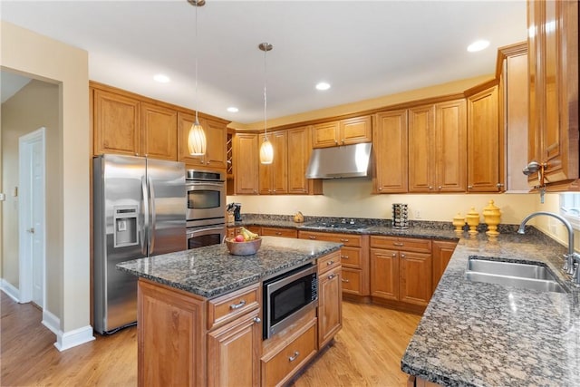 kitchen featuring a sink, under cabinet range hood, brown cabinetry, a kitchen island, and appliances with stainless steel finishes